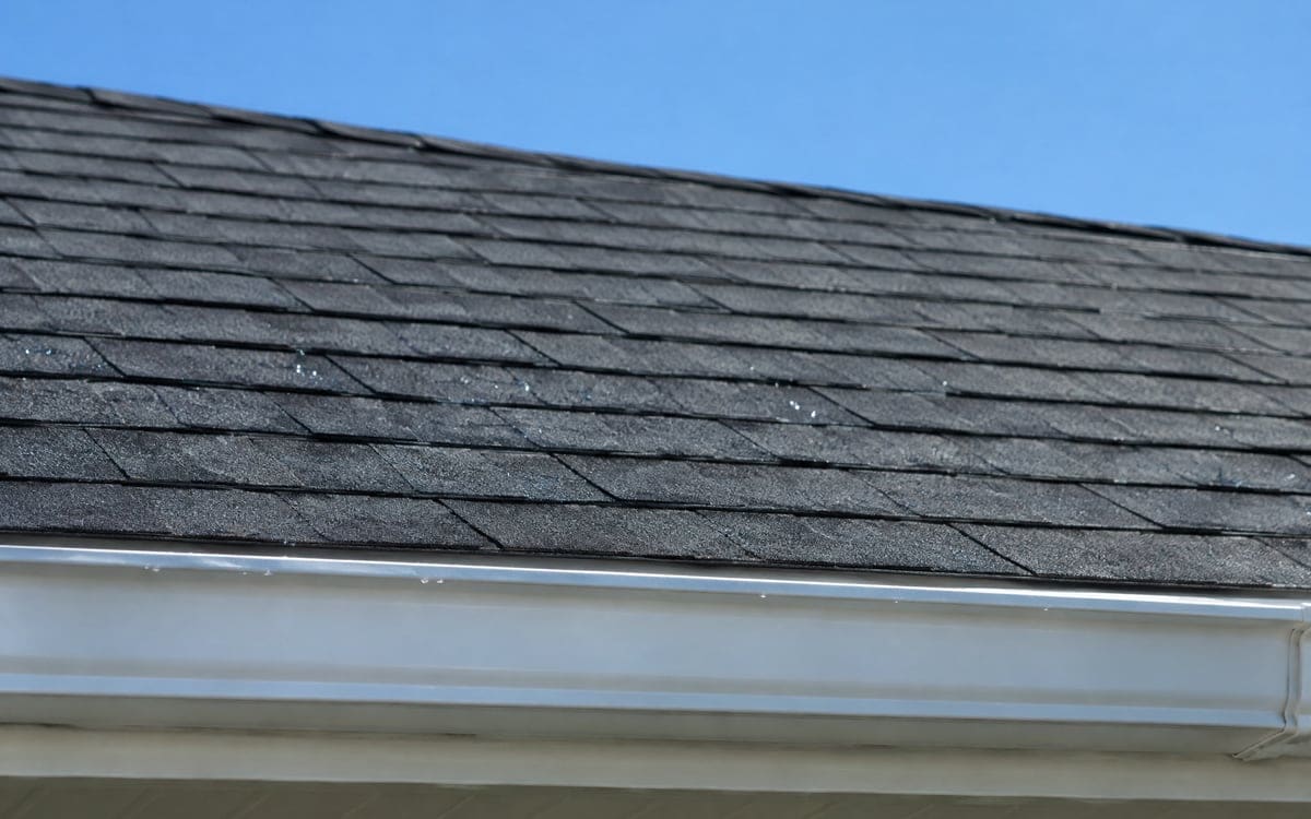 A close look at a dark gray asphalt shingle roof after a cleaning, the courses even in color down to the white aluminum gutter at the eave.