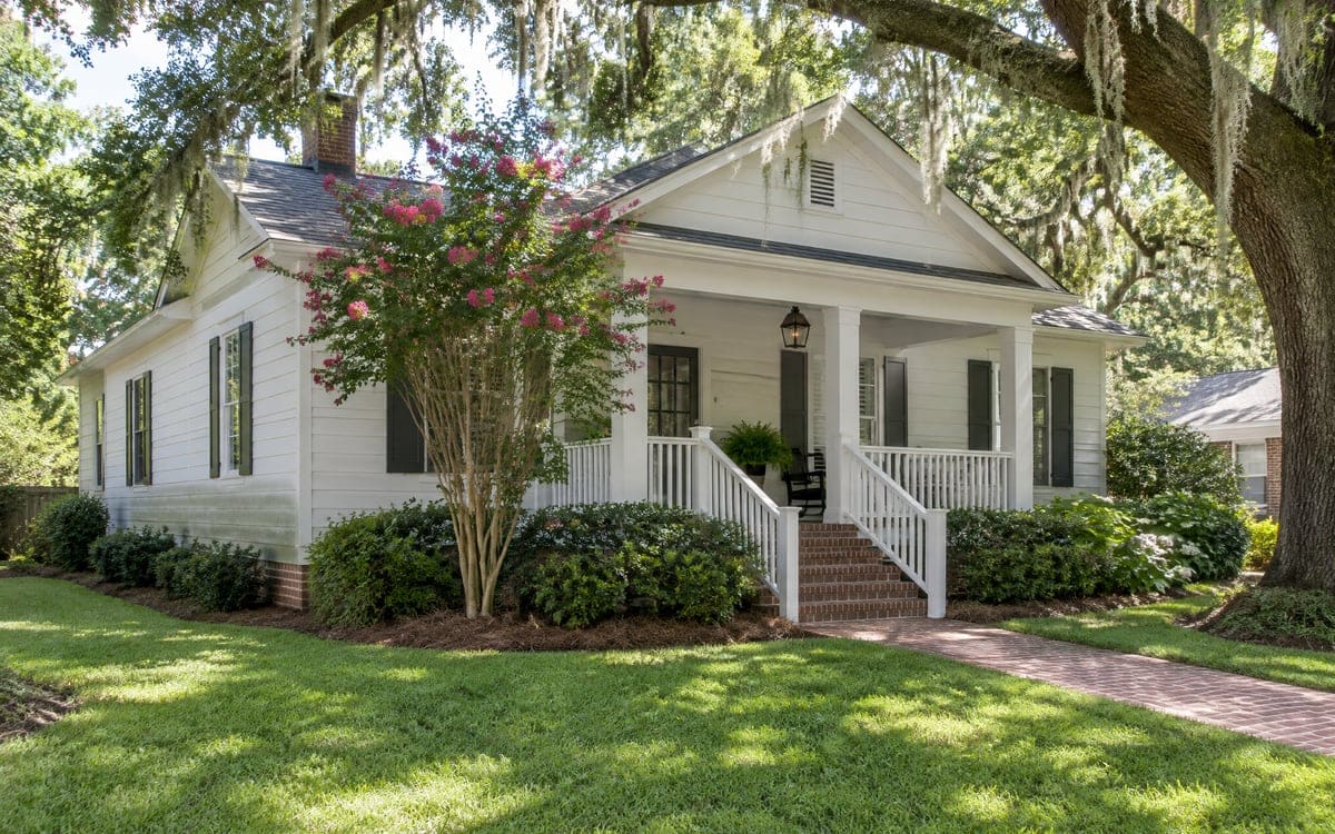 How often to wash a house: a white Baton Rouge raised cottage under Spanish moss, pink crape myrtle at the corner.